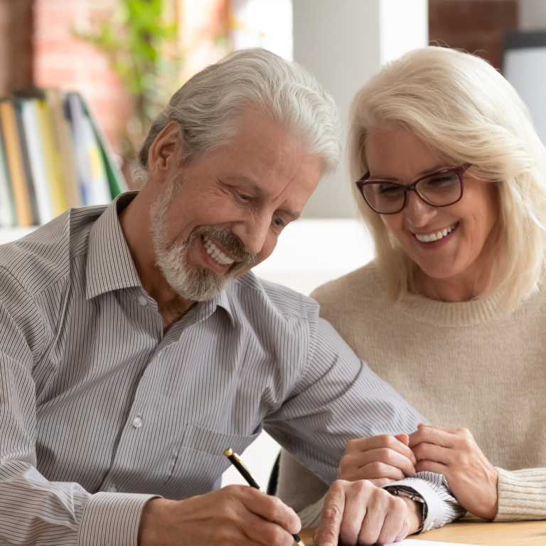 A smiling senior couple reviewing and signing paperwork together