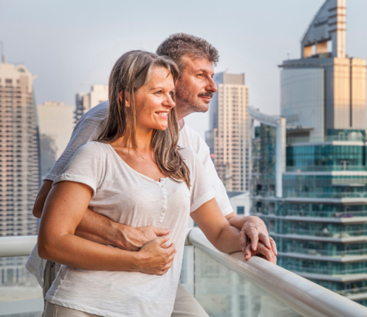 A couple embracing on a high-rise balcony overlooking a city skyline