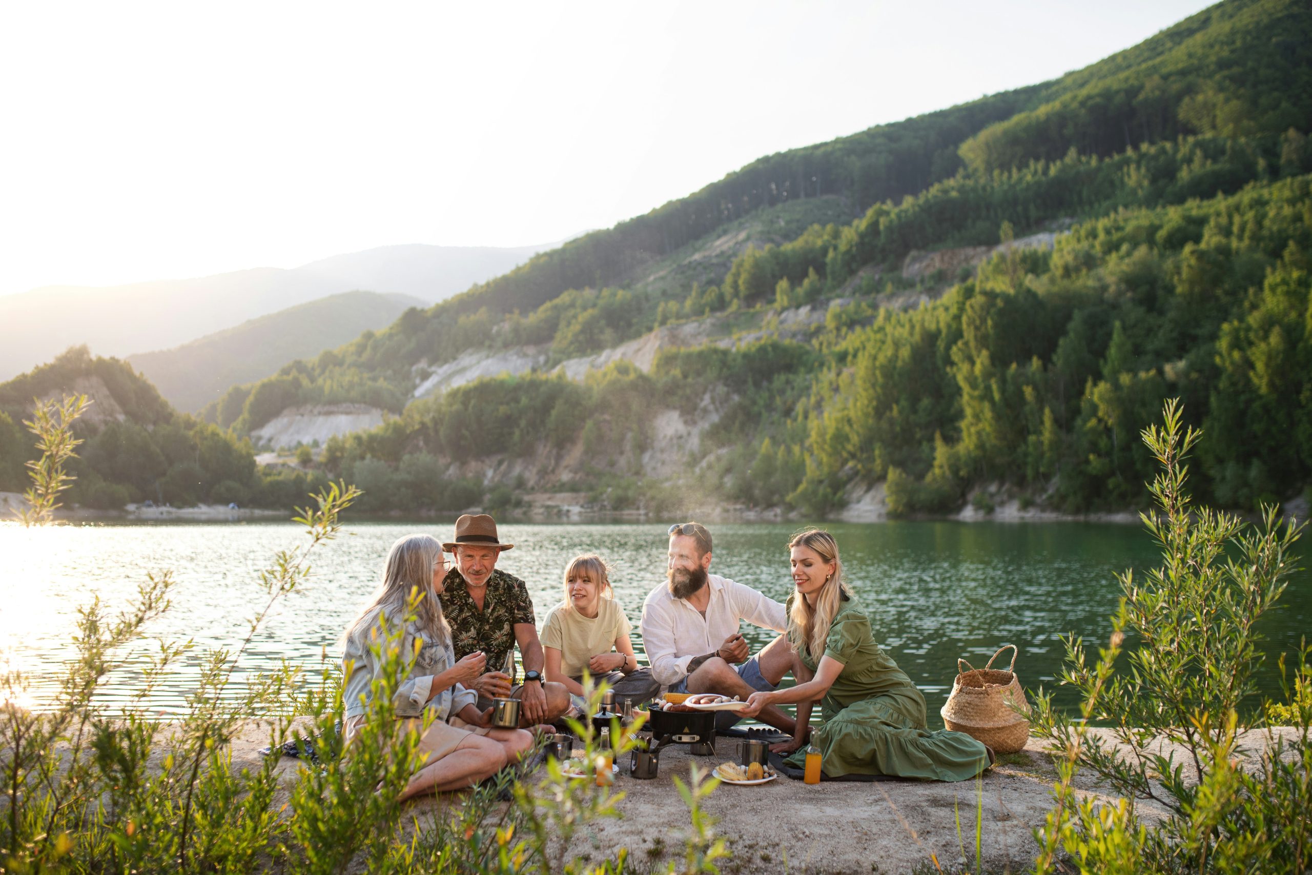 A family sharing a meal together at the edge of a lake at golden hour